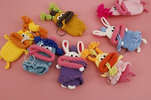 Flat lay of colorful handmade crochet key cases with cartoon designs on pink background