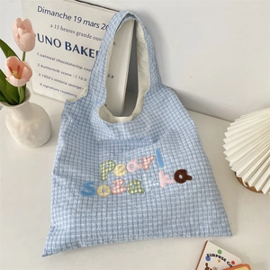 Detail of light blue gingham tote bag featuring colorful Pearl Sozakka letter embroidery