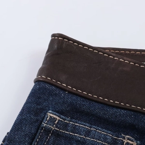 Vue macro de la taille d'un jean bleu foncé avec bordure en cuir brun et coutures bais