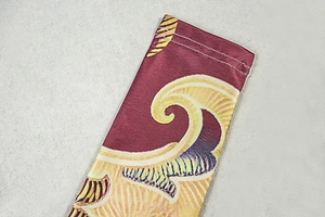 Detailed close-up of double-stitched hem on burgundy and gold printed bodysuit