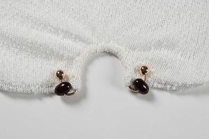 Macro shot of white textured tweed fabric with golden metallic bean-shaped clasp closure