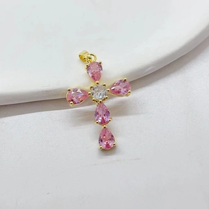 Detailed view of a gold-plated cross pendant with pink teardrop zircons on a white tray