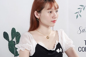 Close-up of a model wearing a gold necklace and earring set with white round enamel charms