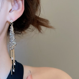 Close-up of golden tassel earrings with square crystals and chain fringes on model