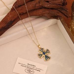Détail du collier croix vintage doré avec émail vert et pierres précieuses bleues