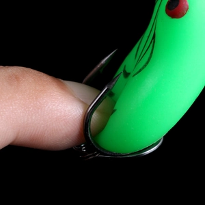 Macro shot of soft green frog lure showing sharp double hooks and flexible body texture