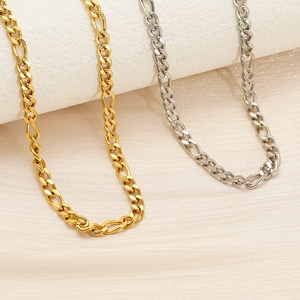 Close-up of gold and silver Figaro chain links on a textured marble and silk surface