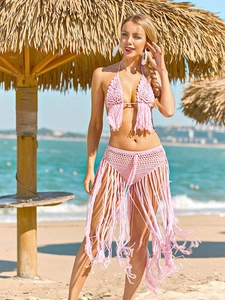 Detail of pink crochet bikini set with handmade tassels against a tropical beach background