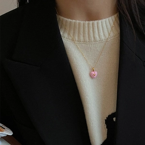 Close-up of a pink enamel heart pendant on a gold chain necklace worn over a white top