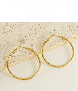 Detailed close-up of large 18K gold plated hoop earrings on textured stone surface