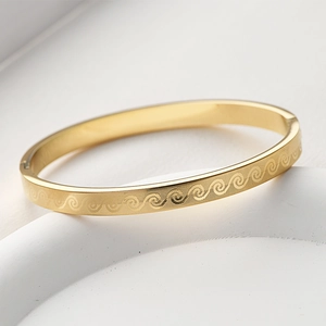 Detailed macro view of gold-finished titanium steel bangle with etched wave patterns
