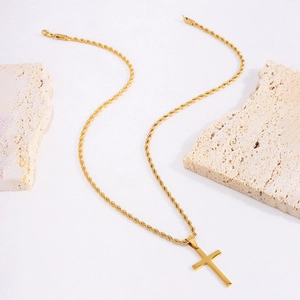 Detailed view of a gold cross pendant on a twist chain atop beige travertine stone