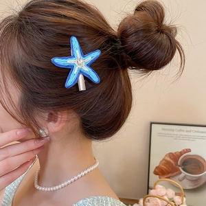 Détail d'une pince à cheveux étoile de mer en raphia bleu avec diamant sur un modèle