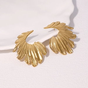 Orecchini a perno a piuma d'oro eleganti in stile artistico su un piatto di ceramica bianca