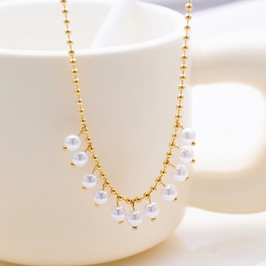 Detailed shot of golden bead chain necklace with white pearl pendants on a white ceramic cup