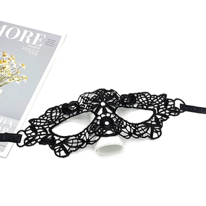 Flat lay of an intricate black lace party mask on white desk with magazine decor