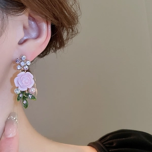 Close-up of earrings featuring pink roses, green leaves and pearls on a model