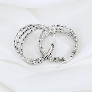 Polished silver stainless steel triple twisted hoop earrings on white silk fabric background