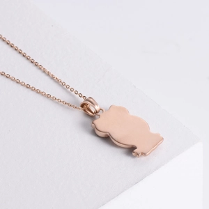 Cute rose gold owl pendant necklace in stainless steel on a white geometric stand