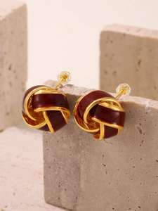 Macro detail of red enamel gold twist knot earrings on natural stone surface