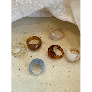 Top view of assorted marble resin oval rings in amber and neutral tones on beige stone