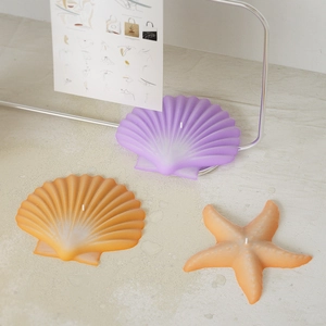 Starfish and seashell scented candles in purple and orange on a minimalist stone surface