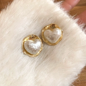 Vista macro degli orecchini a cuore placcati oro 16K con perla bianca e bordo ondulato