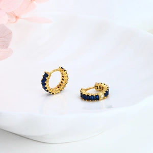Detailed shot of gold hoop earrings with blue zircon stones on a white ceramic plate