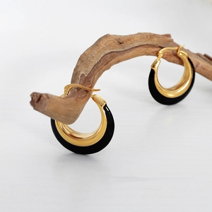 Modern C-shaped hoop earrings with gold metal and black enamel finish on rustic branch