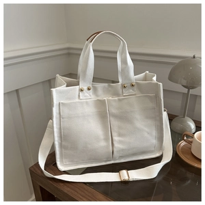 Close-up of white canvas tote bag with large front pockets and adjustable gold-tone strap