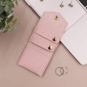 Pink leather jewelry organizer pouch with gold snap and ear stud slots on a desk