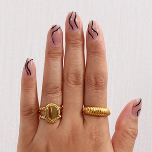 Macro shot of gold oval signet ring and ribbed band on hand with modern nail art