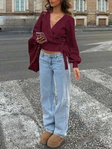 Outdoor street view of a wine red wrap-around tie knit sweater paired with wide-leg jeans