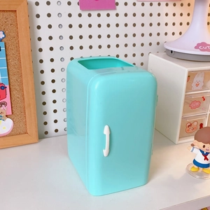 Close-up of a teal mini fridge-shaped desk organizer on an aesthetic white desk