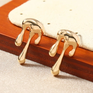Macro shot of gold fluid earrings on wood texture showcasing sleek metallic luster and curves