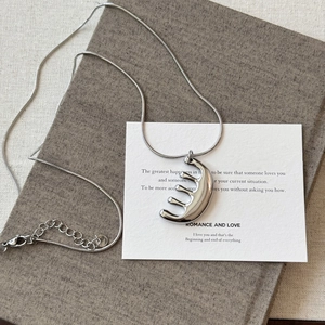 Vue détaillée du collier pendentif peigne argenté sur un livre avec une chaîne serpent élégante