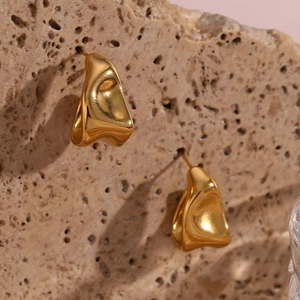 Macro view of gold irregular liquid-metal earrings on natural textured stone background