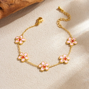 Detailed shot of a gold flower necklace with pink enamel petals on a textured sand surface