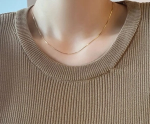 Close-up of a minimalist gold snake bone chain necklace worn by a model to show fit