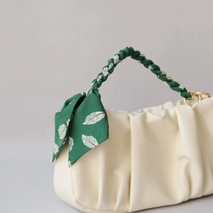 Close-up of cream pleated handbag with green woven handle and leaf print silk scarf detail