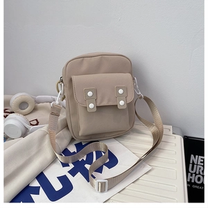 Detail of khaki canvas crossbody bag with double white buttons on a white suitcase