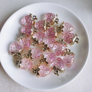 Detailed view of pink resin strawberry pendants with gold leaves in a white ceramic dish