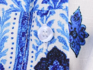 Primer plano de tela con estampado floral geométrico y botón blanco en vestido camisero