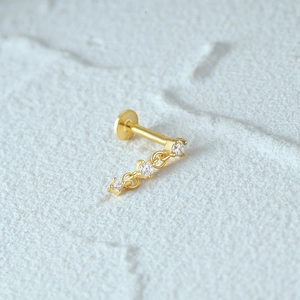 Macro shot of 16G gold cartilage stud with internal threading and three clear gemstones