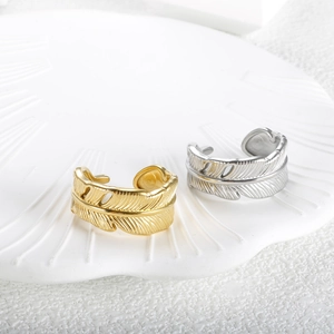 Adjustable feather-shaped open rings in gold and silver finish on a white shell tray