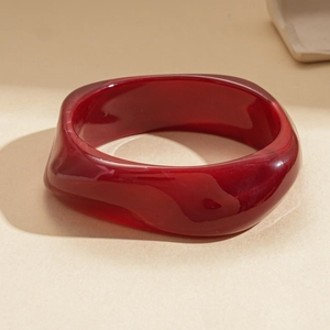Détail macro du bracelet en acrylique rouge foncé translucide au design ondulé torsadé