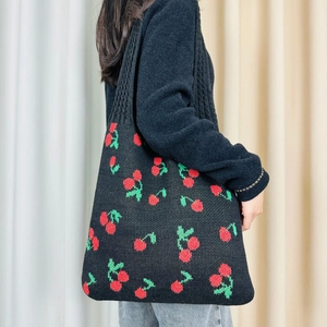 Detail of black knitted tote bag featuring red and green cherry patterns on shoulder
