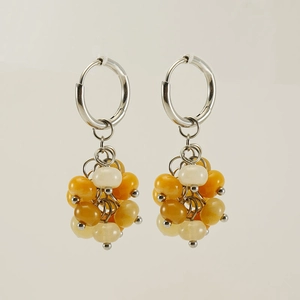 Gros plan de boucles d'oreilles avec perles en pierre naturelle jaunes et blanches sur beige