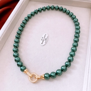 Close-up of dark green pearl necklace with gold-plated zircon buckle on beige tray