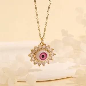 Detail of 18K gold plated evil eye necklace with pink and blue stones on sand background